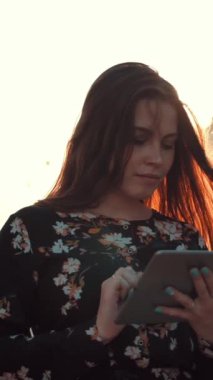 Dijital bloknotu olan çekici genç bir kız internette geziniyor. İlginç bir şey bulmaya çalışıyor. Gerçek zamanlı ve ağır çekimde. Sabah güneş doğarken. Dikey çekim.