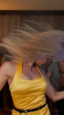 Sarışın kadın parti dansçısı. Dans pistinde dans eden oldukça neşeli, neşeli, sarışın bir kadın. Arkadaşları da müzikle zıplıyorlar. Ağır çekim. 4k dikey çekim.