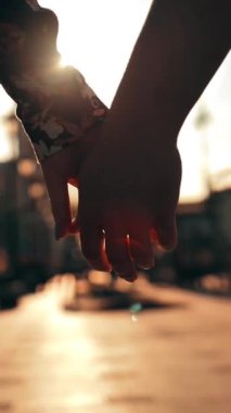 Şehrin gün batımında güzel bir mercek ışığıyla el ele tutuşan iki el. Erkek ve dişi aşıklar kollarına dokunuyor. Süper yavaş çekim. Dikey çekim.