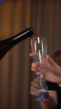 Yakışıklı bir adam şampanya dolduruyor. Gece elbiseli iki çekici seksi kızın bardaklarına köpüklü şarap koyuyor. Yakın plan. Dairede rahat bir parti. 4k UltraHD. Dikey çekim.