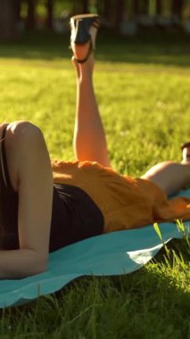 Mutlu, genç, yakışıklı seksi kadın yeşil çimlerin üzerine uzanmış telefonda mesaj yazarken ve neşeyle sallanırken. Dikey çekim.
