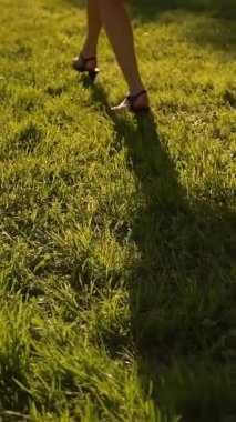 Parkta çimenler tarafından yönetilen kadın ayakları. Yüzü yok. Gün batımı ya da yüzey. Süper yavaş çekim. Orta etek, ince bacaklar. Dikey çekim.