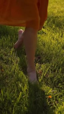 Parkta çimenlerin üzerinde koşan kadın ayakları. Yüzü yok. Gün batımı ya da yüzey. Süper yavaş çekim. Orta etek, ince bacaklar, yalın ayak. Ön taraf, yakın plan. Dikey çekim.