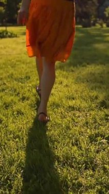 Parkta çimlerin üzerinde koşan kadın ayakları. Yüzü yok. Gün batımı ya da yüzey. Ağır çekim. Orta etek, ince bacaklar, yalın ayak. Dikey çekim.