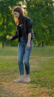 Genç bir kadın, köpeğini havaya katlamak için bir tenis topu fırlatıyor. Evcil bir hayvanla eğlenceli bir oyun. Komik bir safkan köpek topu yakalamak için zıplar ve şehir parkındaki metresine tenis topu getirir.