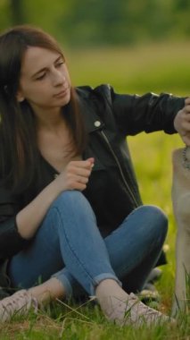 Kadın, parkta köpeğini yaka paça okşuyor. Çayırda köpeği olan çekici bir kız, köpeğinin kafasını okşuyor. Evcil hayvan konseptine bayılırım. Orta yavaş çekim. Dikey çekim.