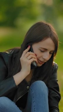 Parkta bir köpekle yürürken telefonda konuşan bir kız. Ortalama bir plan, güzel bir kadının elinde cep telefonu tutması. Köpeğin yanında duruyor. Dikey çekim.