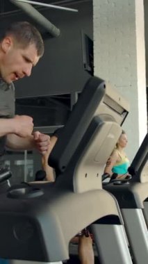 Modern bir spor kulübünün penceresinin yanındaki koşu bandında antrenman yapan ve koşan bir grup sporcu. Yan geniş görünüm dikey çekim.