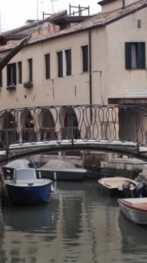 Kırmızı elbiseli kadın Venedik 'te köprüden atlıyor. Tekneler, nehir ve tarihi binalar. Dikey çekim.