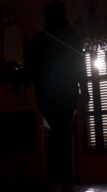 Kadın odada panjurları açıyor. Güzel bir bayanın silueti sabahın ilk ışıklarına hayran kalıyor. 4K UHD. Dikey çekim.