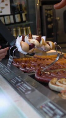 Sosisli sandviç küçük market ayrıntıları. Satıcının ve müşterinin elleri. Sosis ve ekmek dikey çekim.