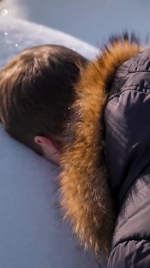 Kışlık ceketli bir adam kar yığınında yüzünün bir kopyasını yapar. Güneşli bir kış haftasonunda kaygısız bir eğlence. Dikey çekim.