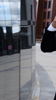 Girişimci şehir ticaret bölgesinde cep telefonuyla konuşuyor. Akıllı telefondan konuşan kendinden emin genç bir iş adamı. Kahve molası. Süper yavaş çekim. 240 fps dikey atış.