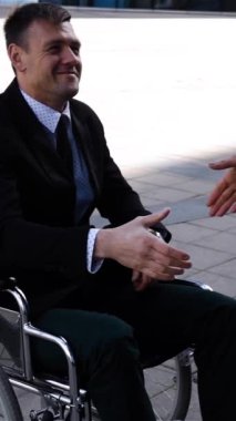 Resmi takım elbiseli iş kadını, engelli iş adamıyla el sıkışıyor. Gün batımında havalı, modern bir iş merkezi binası. Süper yavaş çekim. Yüksek hız fps 250 kameramanlı gün