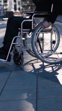 Fiziksel engelli iş adamı. Tekerlekli sandalyesini çok yavaş çekimde kameraya çeviriyor. Modern cam iş alanı geçmişi. Geniş destansı çekim. Tarafsız duygular. Dikey çekim.