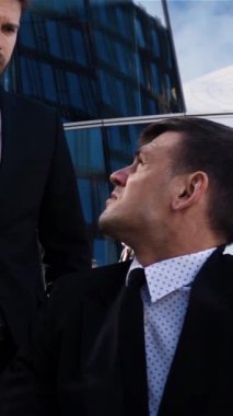 Çekici iş adamı, engelli çalışanını, sakat tekerlekli sandalyesinde cam odun binasının dışında otururken kovuyor. Sakat adam kavramından kovuldun. Ağır çekim. Dikey çekim.
