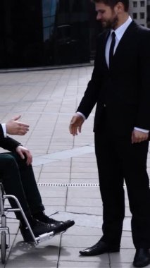 Tekerlekli sandalyedeki sakat iş arkadaşıyla ağır çekimde tokalaşan mutlu girişimci. Gün batımı ya da gün doğumu. Mutluluk. Servet ve konforlu çalışma ve ortaklık dikey çekim.