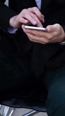 İphone ile çalışan erkek işadamı, fiziksel engelli adam iş yeri bölgesinde tekerlekli sandalyede oturuyor, insanlar ve handikaplar, tekerlekli sandalyede gelecek için inanç. Kollar yakın çekim. Dikey çekim.