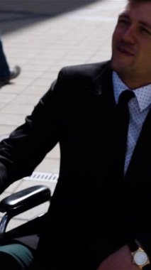 Tekerlekli sandalyedeki engelli iş adamıyla ağır çekimde tokalaşan mutlu girişimci. Teal ve turuncu stil. Güneşli bir gün. Mutluluk. Modern iş merkezi bg Dikey çekim.