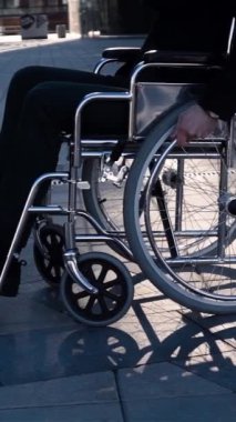 Tekerlekli sandalyeli bir iş adamının yavaş çekim görüntüsü. Yürüyor, dönüyor ve iş meydanındaki kameraya bakıyor. Mutlu gülümseyen engelli adam. Orta görünüm dikey çekim.