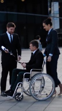 Tekerlekli sandalyedeki iş adamı, bayan yönetici ve ortak girişimci ile dışarıda görüşürken. Engelli insanlar iş başında. 4k ultra hd. geniş dikey çekim.