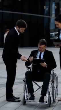 Patron sakat tekerlekli sandalyede ve onun iş kadını elinde iş yerinin dışındaki ortağının imzalı evrakları var. 4k ultra HD. Dikey çekim.