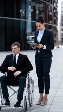 Geçersiz tekerlekli sandalyede başarılı bir patron ve iPad 'li bir işvereni. Açık hava sekreteri konseptinde gadjetler ile çalışmak. Tablet PC veya Dijital Pad aygıtı. Dikey çekim.