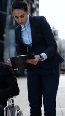 Genç girişimci kötürüm iş adamı sakat tekerlekli sandalyedeki kadın meslektaşı sekreter asistanıyla metindeki belgeler hakkında iletişim kuruyor. Dikey çekim.