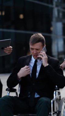 Tekerlekli sandalyedeki bir iş adamı ofis binasının dışında iş arkadaşlarıyla anlaşmaları tartışıyor. Metin defteri, dijital ped, iPhone ve belgelerle çalışıyorlar. Özürlüler topluluğun bir parçası. Dikey