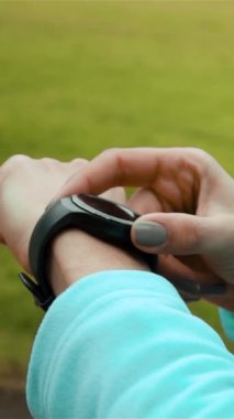 Koşucu, ormanda koşarken akıllı saat fitness takip cihazı ve kalp atış hızı monitörü kullanıyor. Koşu parkında egzersiz yaparken kardiyo eğitimi verilerini kontrol eden bir kadın sporcu. Dikey çekim.