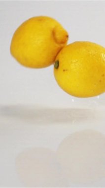 Lezzetli limonlar ıslak beyaz yüzeyde zıplıyor ve zıplıyorlar. Ağır çekim modunda yüksek hızlı kamerayla çekildi. Limonlar kamerada çok hızlı hareket eder. Beyaz siklonama bg dikey çekim.