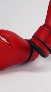 Yavaş çekimde kırmızı deri boks eldivenleri düşüyor ve beyaz arka planda zıplıyor. Dikey Çekim.