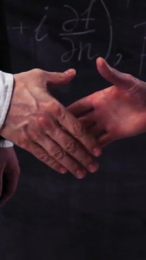 İki bilim adamı karatahtadaki matematiksel denklemlerle tokalaşıyorlar. Süper yavaş çekim. Dikey Çekim.