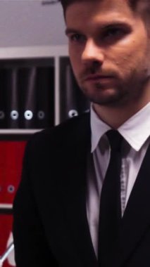 Çekici ve kendinden emin bir işadamı ofis binasının içinde yürüyor. Ağır çekimde. Resmi takım elbise ve kravat. Ofis mobilyaları ve bilgisayar. Dikey Çekim.