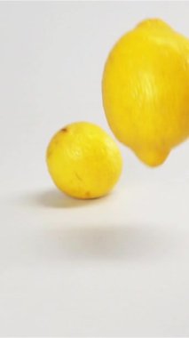 Gri yüzeye dökülen beyaz ekran b.k içindeki birkaç taze sarı limon. Limon yavaş çekimde sıçrıyor. Stüdyo ışıkları. Yakın plan dikey çekim.