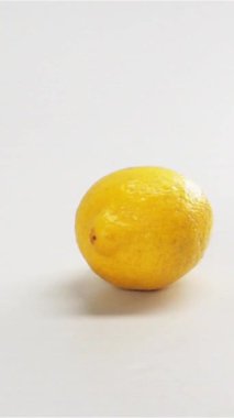 Beyaz masa zemininde parlak ekran bg falli izole edilmiş sarı limon. Limonlar yavaş çekimde sıçrıyor. Stüdyo ışıkları. Yakın plan dikey çekim.