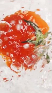 Ağır çekim. Lezzetli, ıslak, kırmızı domates büyük bir sıçrama ve spreyle suya dalıyor. Dikey makro görünüm. Dikey Çekim.