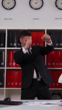 4K, genç, çekici, seksi iş adamı ofiste ayakta ve dans ediyor. monitör bilgisayar, dijital ped, klavye, cep telefonu. Dikey Çekim.