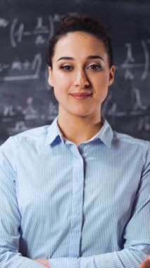 Arkaplanda matematik denklemleriyle dolu tebeşirle ayakta duran zeki kadın öğretmen portresi. Kollarını kavuşturup gülümseyen bir kadın. Glidetrack Dikey