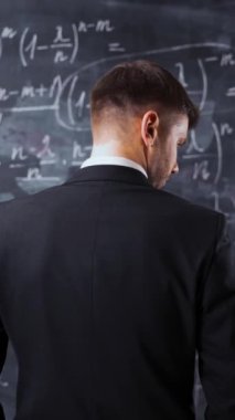 Erkeğin tebeşir tahtasına karşı matematiksel formül denklemleri ile arka orta pozu. Çözümleri düşünüyor ve üniversite görevlerini anlamaya çalışıyor. Dikey Çekim.
