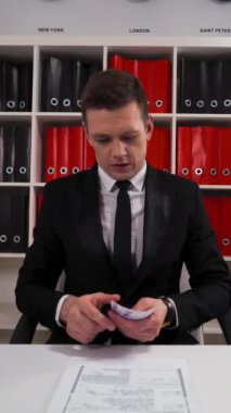 Siyah takım elbiseli ve kravatlı yakışıklı işadamı. Söz verme işi ve hizmet yerine getirilecek. Parayı iç cebine sakla. Ofis içinde. Teal ve Orange. Dikey Çekim.