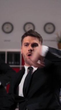 Resmi takım elbiseli üç neşeli üniversiteli ofiste neşeyle dans ediyor. Yakışıklı adammış. İş yerindeki kulüp partisinden sonra. Dikey Çekim.