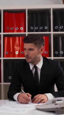 Resmi siyah takım elbiseli bir iş adamı rakip hakkında bilgi sızdırmaya çalışıyor ama boks eldivenini yüzüne yapıştırıyor. Ofis beyazının içinde. Dikiz konsepti. Ultra HD Dikey Çekim.