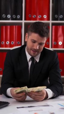 4k UHD. Çekici genç işadamı elinde dolarları tutuyor ve sayıyor..