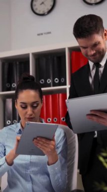 Resmi takım elbiseli genç ve çekici iş arkadaşları ofiste dijital tabletlerle çalışıyorlar. Kaydırma kamerası hareketi. Dikey Çekim.