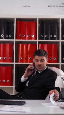 Ofiste çalışan başarılı genç iş adamı telefonla konuşuyor ve bilgisayarın klavyesini dijital kağıt grafikleriyle daktilo ediyor. Mutlu görünüyor ve çok gülümsüyor. Glidetrack kaydıracı atışı