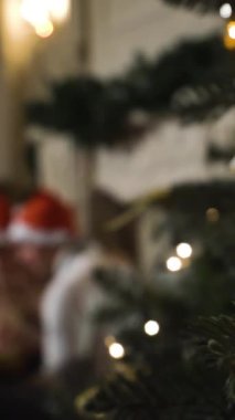 Noel 'i kutlayan güzel çift. Bir fotoğraf albümü yapmayı düşünüyorum. Bulanık bg. Parlak renkli ışıkları olan bir Noel ağacı. Kırmızı ve beyaz şapkalar. Dikey Çekim Odaklı Ağacın İlk Planı.