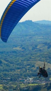 Süper yavaş çekim. İki kişi Paramotor paraşüt paraşüt uçağına biniyor. Gün ortası güneşli dağlarla gökyüzünde uçuyorlar. Mavi bulutlar. Dikey çekim.