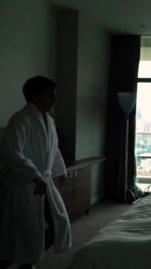 Ağır çekim. Otelde bornozlu mutlu adam yatağı. Kocaman bir pencere. Güzel daireler, rahatlama. Sıkı çalıştıktan sonra rahatlama kavramı. Tatil günü. 250 fps Dikey Vuruş.