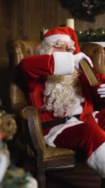 Noel Baba Noel arifesinde koltukta otururken yeşil yılbaşı ağacının yanında oyuncakları ve ışıkları olan kırmızı ipek bir albüm çıkarır. Geniş açılı kaydırma doli hareketi Dikey Çekim.